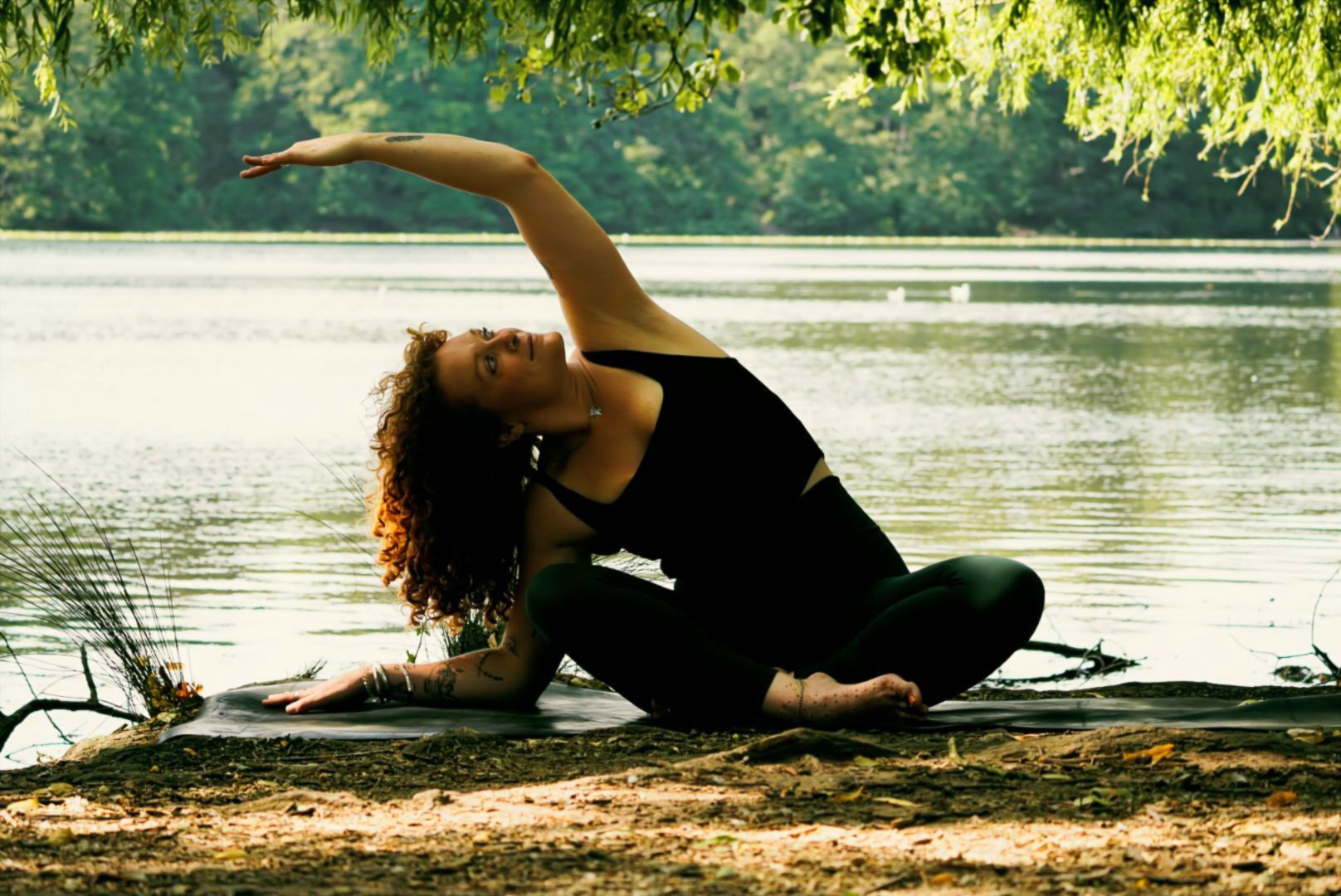 Grace in a seated side stretch on a mat by the water