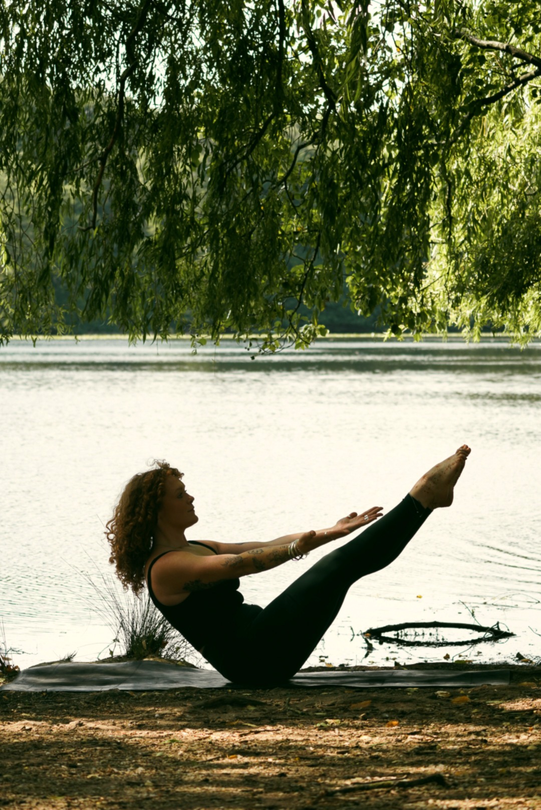 Grace in boat pose under willow trees by the lake