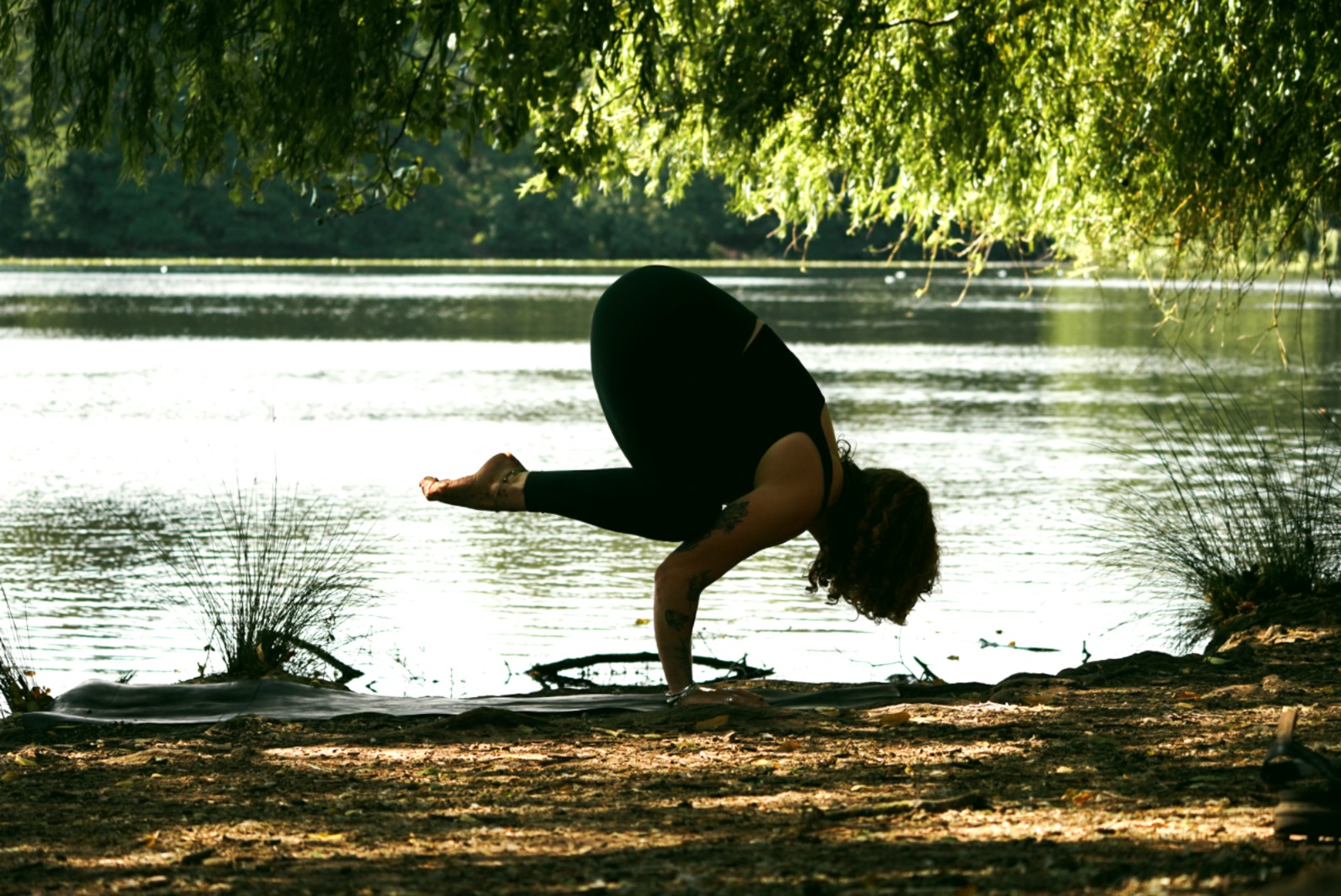 Grace in crow pose on a mat by the lake